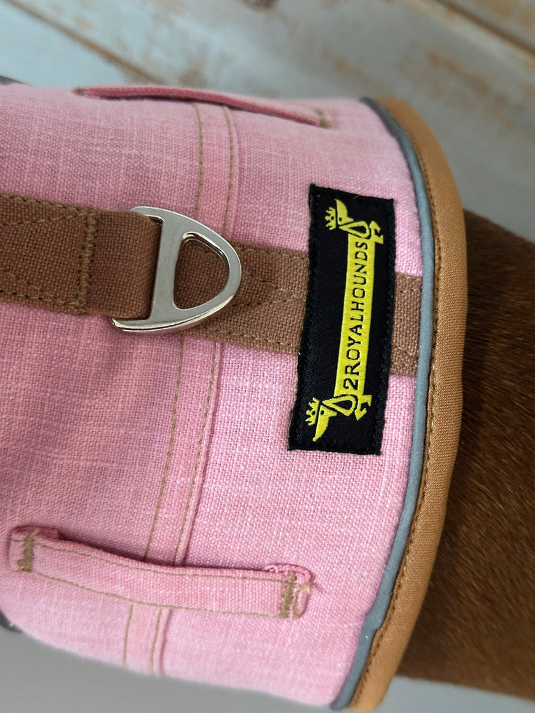 Pink dog harness with a brown strap and visible brand label on a blurred background